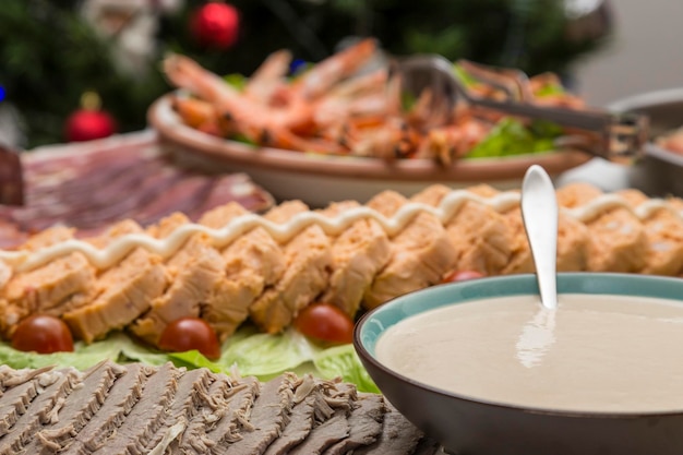 Tazón con salsa en primer plano platos con comida preparada para una fiesta pastel de pescado carne fiambres mariscos en el fondo y un árbol de Navidad