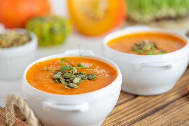 Un tazón de sopa de calabaza con semillas en un fondo de madera blanca de cerca