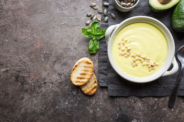 Tazón de sopa de crema de brócoli y guisantes en un tazón blanco con aguacate, vista superior