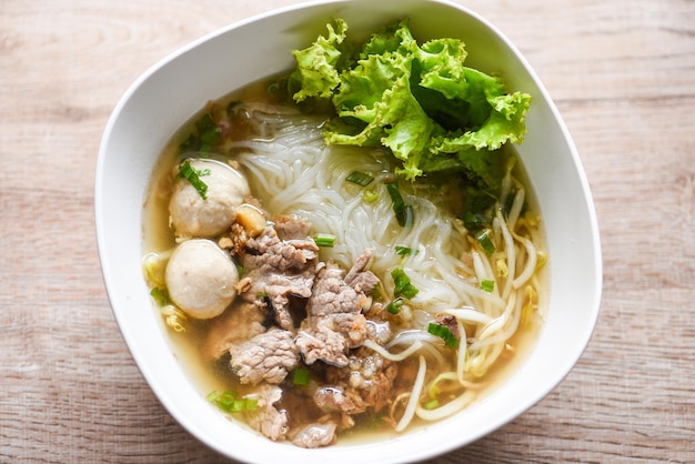 Tazón de sopa de fideos verduras frescas lechuga cerdo y bolas de cerdo sobre fondo de madera Comida de menú tradicional tailandesa