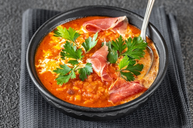 Tazón de sopa de lentejas, tomate y coco con jamón serrano