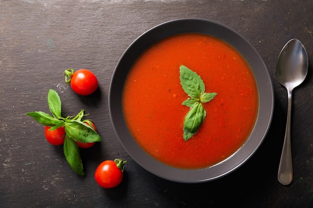 Tazón de sopa de tomate con albahaca sobre fondo oscuro