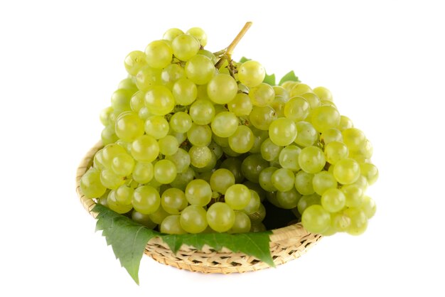 Un tazón de uvas blancas sabrosas, maduras con el fondo blanco.