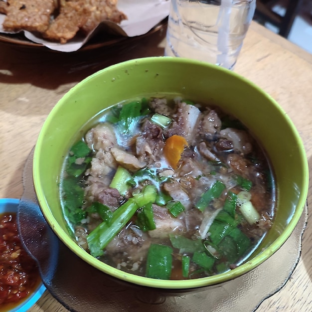 Un tazón verde de sopa con una salsa roja al lado.