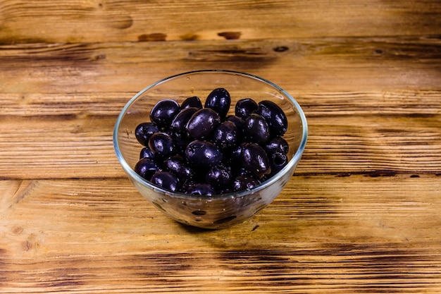 Tazón de vidrio con aceitunas negras sobre mesa de madera rústica