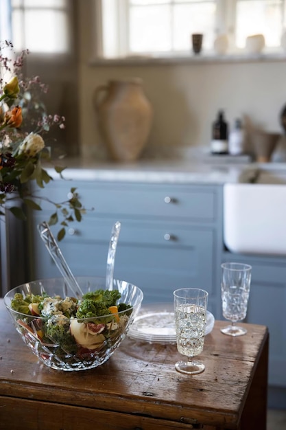 Tazón de vidrio con ensalada vegetariana fresca y vasos para beber en el interior de la cocina