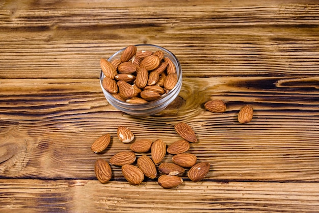 Tazón de vidrio con nueces de almendras peladas sobre mesa de madera