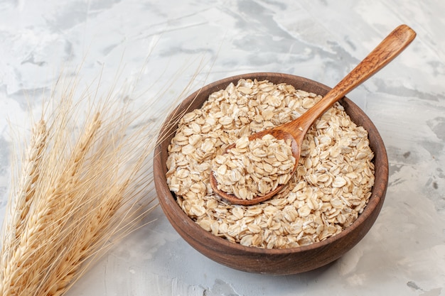 Tazón de vista inferior con avena y espigas de trigo de cuchara de madera sobre fondo gris