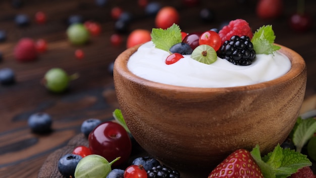 Tazón de yogur con frutas del bosque en la mesa de madera oscura