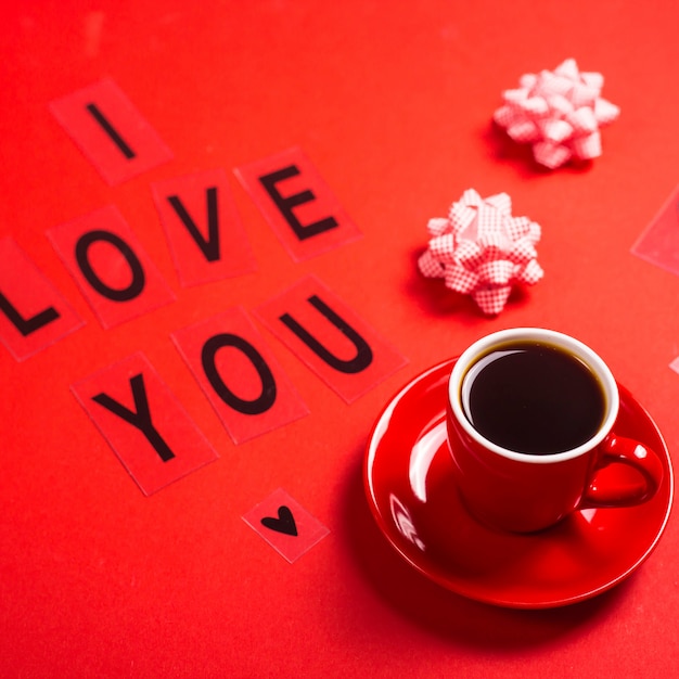 Te amo escrito en letras negras sobre un fondo rojo brillante al lado de una taza de café expreso roja