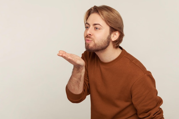 Te amo querida. retrato de homem bonito com cabelo arrumado e barba vestindo moletom, enviando beijo de ar romântico