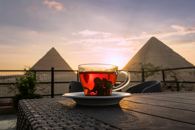 Té árabe tradicional en un vaso con el telón de fondo de las Grandes pirámides de Giza. Hermosa vista de la atracción en el restaurante al atardecer. El sol se pone detrás de las pirámides