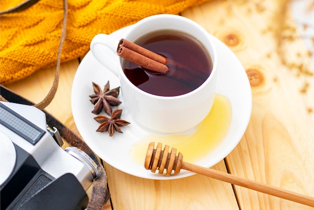 Té aromático de canela caliente cubierto con un cálido pañuelo sobre un fondo de madera de otoño. cazo de miel con miel. cómodo leyendo un libro. la cámara está en el fondo