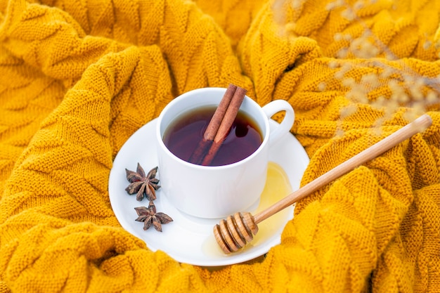 Té aromático de canela caliente cubierto con un cálido pañuelo sobre un fondo de madera de otoño. cazo de miel con miel