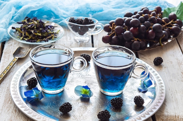 té azul en tazas transparentes, moras y uvas, una cuchara para té y soldadura