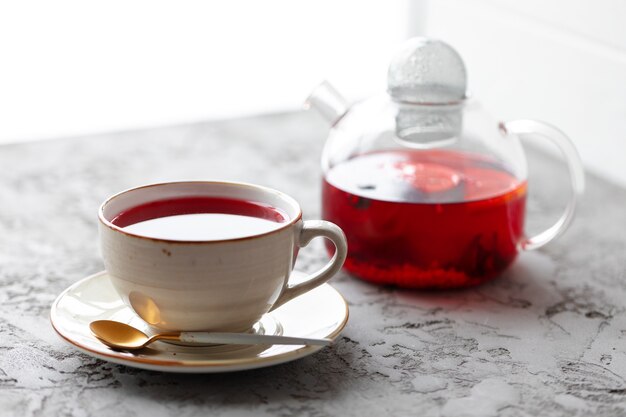 Foto té de bayas en tetera de vidrio sobre superficie gris