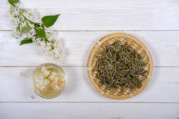 Té blanco chino en plato de bambú y flores lilas blancas sobre fondo de madera