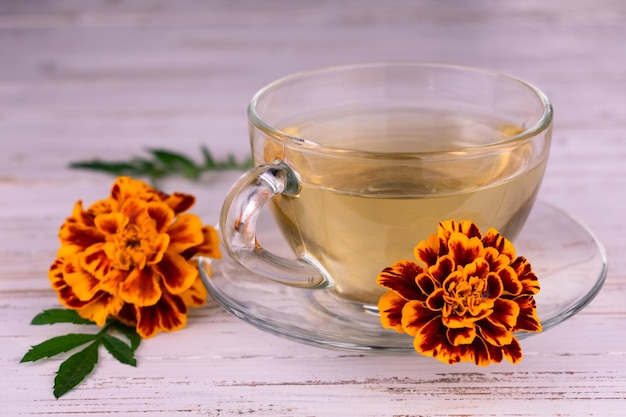 Té de caléndula medicinal en una taza transparente sobre un fondo de madera blanca