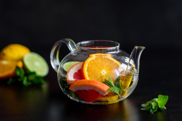 Té caliente de frutas con limón, menta, naranja, lima y pomelo en una hermosa tetera de vidrio