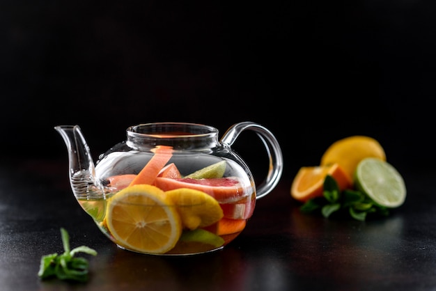 Té caliente de frutas con limón, menta, naranja, lima y pomelo en una hermosa tetera de vidrio