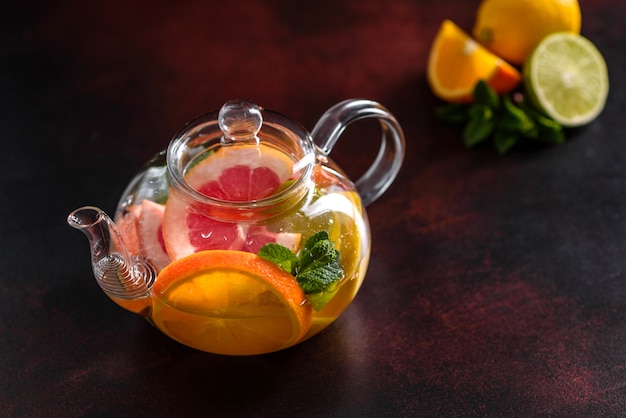 Té caliente de frutas con limón, menta, naranja, lima y pomelo en una hermosa tetera de vidrio