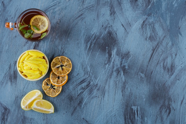 Té caliente con limones y tazón de fuente amarillo de caramelos amarillos sobre fondo azul.