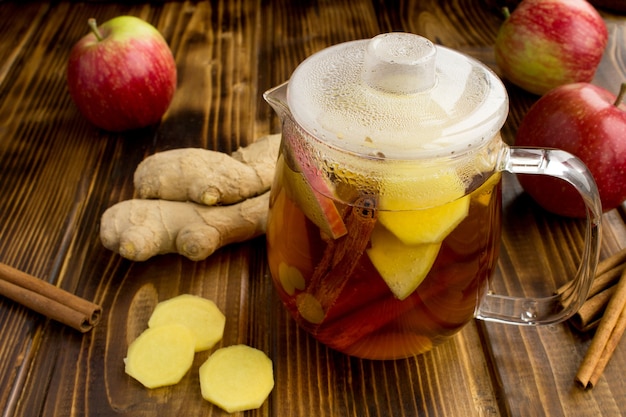 Té caliente con manzanas, canela y jengibre en la tetera de cristal sobre el fondo de madera marrón. Bebida saludable.