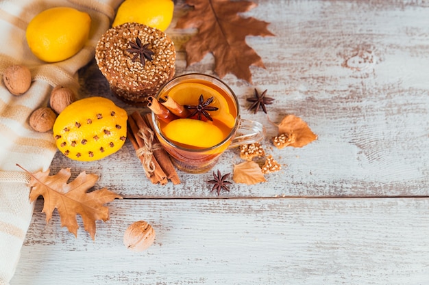 Té caliente de otoño con limón y especias en vaso. Té saludable con galletas, nueces y hojas alrededor. Concepto de otoño