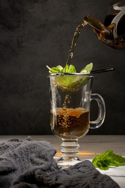 El té caliente se vierte en una taza transparente sobre un fondo negro.