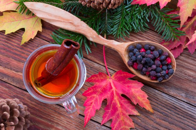 Té con canela y limón, coloridas hojas de otoño de arce, bayas de espino en una cuchara de madera