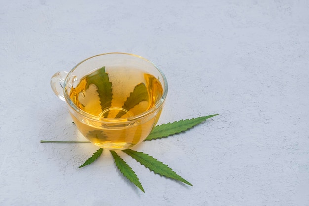 Té de cannabis en una taza de vidrio con hoja de marihuana sobre un fondo de hormigón neutral con espacio para copiar