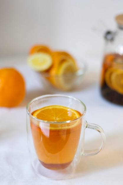 Té de cítricos en una taza de vidrio con doble fondo contra el fondo de una tetera y naranjas