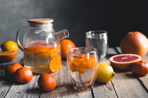 Té de cítricos en una tetera transparente sobre una mesa con pomelo y sobre una mesa de madera