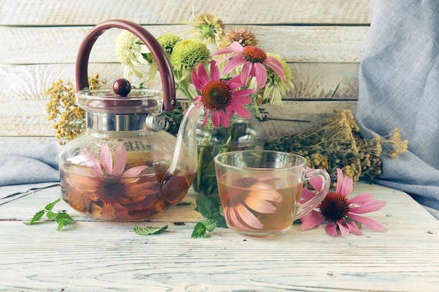 Té curativo de flores frescas de equinácea y menta, en una taza de vidrio y tetera, sobre una mesa de madera