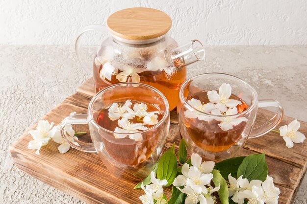 Té curativo de tavya con flores de jazmín en un hervidor de vidrio y tazas sobre un tablero de papel tapiz de madera y fondo de cemento, el té más popular