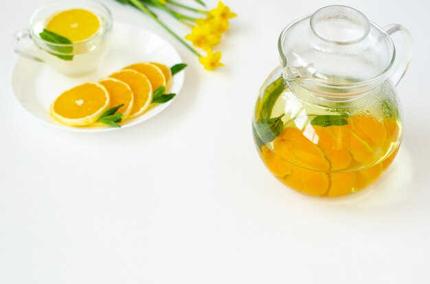 Té desintoxicante en tetera transparente con fruta naranja y menta y flor amarilla Narciso