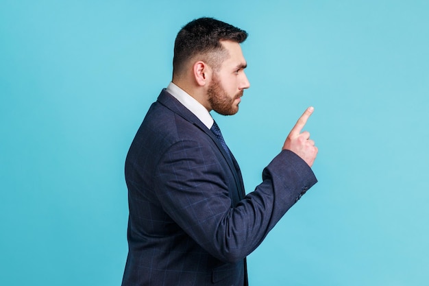 Te dije. Retrato de vista lateral de un hombre serio con traje de estilo oficial, de pie con el dedo índice levantado mostrando un gesto de advertencia, tenga cuidado. Disparo de estudio interior aislado sobre fondo azul.