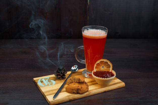 Té dulce sabroso con sabor a rojo caliente con mermelada de fresa y galletas de avena se encuentra en una mesa de madera vintage en un café. Bebida tibia dulce. Ambiente acogedor.