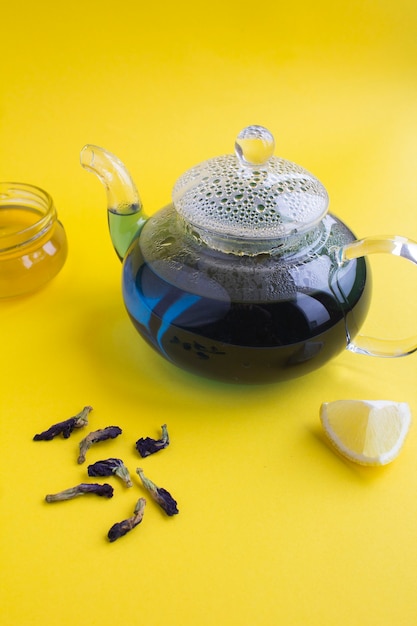 Té de flor azul en la tetera de cristal sobre el amarillo