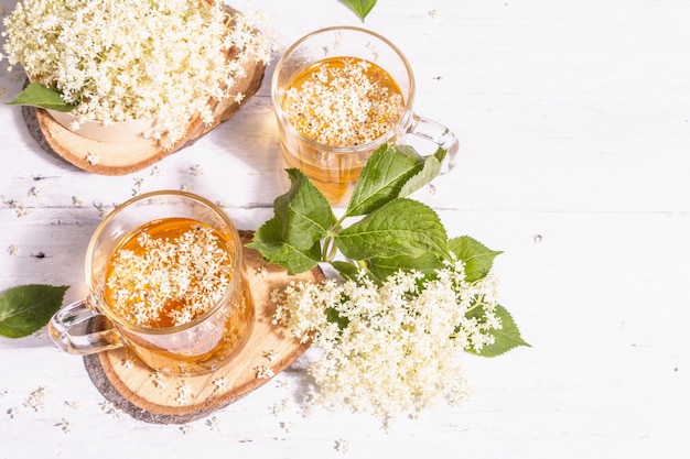 Té de flor de saúco. Bebida refrescante de verano, concepto de estilo de vida saludable. Luz dura de moda, sombra oscura. Viejo fondo de tablas de madera blanca, vista superior