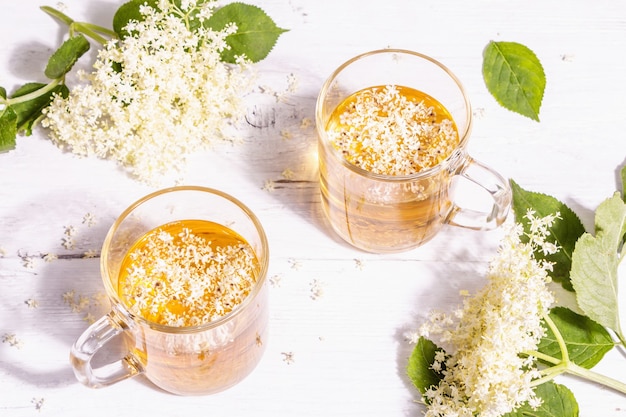 Té de flor de saúco. Bebida refrescante de verano, concepto de estilo de vida saludable. Luz dura de moda, sombra oscura. Viejo fondo de tablas de madera blanca, vista superior