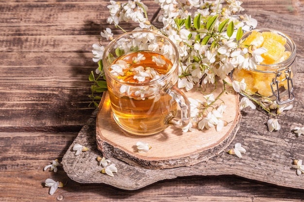 Té de flores de acacia. Bebida de vitamina saludable de verano, luz dura, sombra oscura. Miel dulce, soportes de madera antiguos, espacio de copia