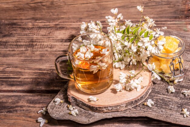 Té de flores de acacia. Bebida de vitamina saludable de verano, luz dura, sombra oscura. Miel dulce, soportes de madera antiguos, espacio de copia