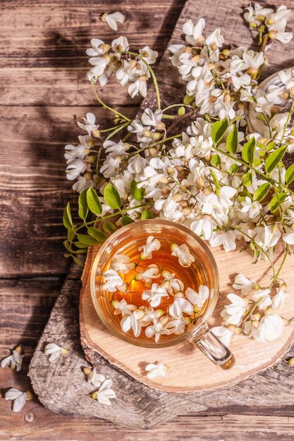 Té de flores de acacia. Bebida de vitamina saludable de verano, luz dura, sombra oscura. Miel dulce, soportes de madera antiguos, vista superior