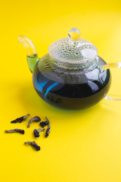 Té de flores azules en la tetera de cristal sobre la mesa amarilla. Copie el espacio.