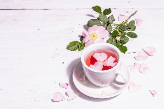 Té de flores de escaramujo. Bebida de vitamina de verano, luz dura, sombra oscura. Fondo de madera blanca, espacio de copia