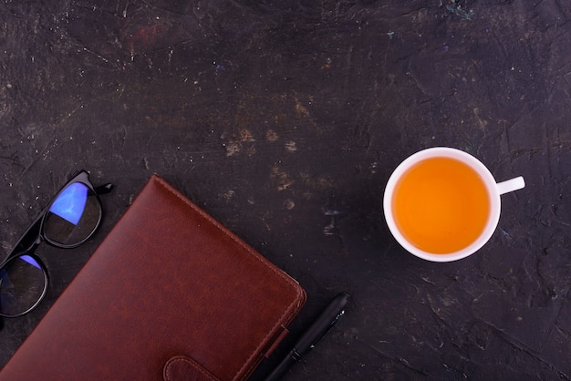 Té fragante en una taza blanca, un cuaderno con un bolígrafo y vasos.