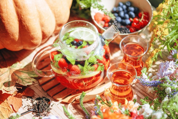 Té de frutas aromáticas naturales en una tetera transparente y en una taza entre bayas y flores té aromático cálido con un profundo aroma a bayas y flores silvestres