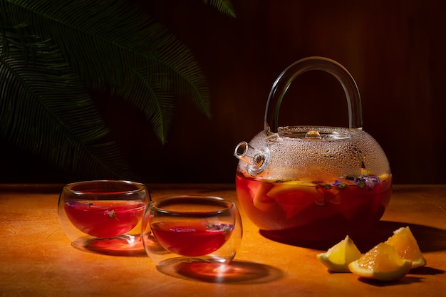 Foto té de frutas con flores de malva seca de limón naranja en una tetera de vidrio y dos tazones en la pared naranja