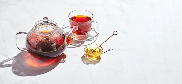 Té de frutas con manzanas y tomillo y miel en tetera de vidrio y taza sobre fondo blanco con sombras duras